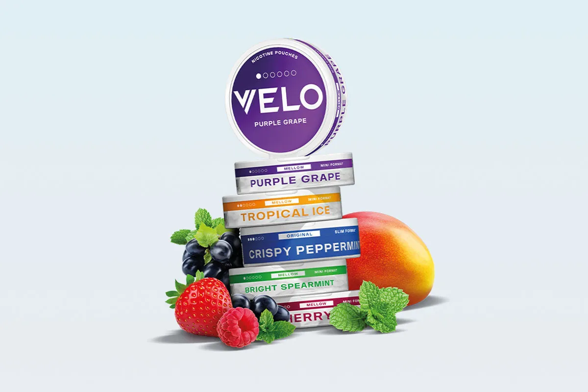 Stack of VELO flavour cans, Purple Grape, Tropical Ice, Crispy Peppermint and Bright Spearmint, with fresh berries, mango and mint leaves